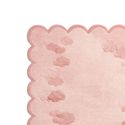 A close-up of a light pink textured rug with a scalloped edge and subtle cloud-like raised patterns, shown on a white background.