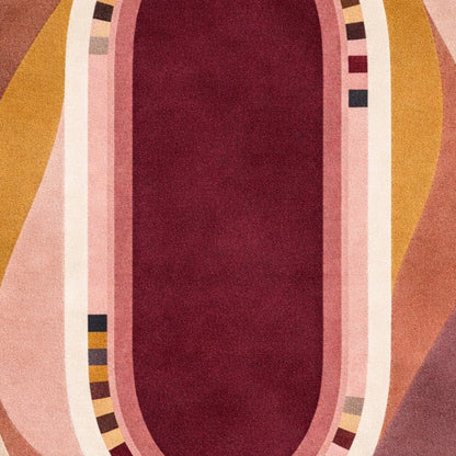 A close-up of a patterned textile or rug featuring a central deep burgundy oval bordered by pink, cream, mustard yellow, and mauve wavy stripes with small geometric accents.