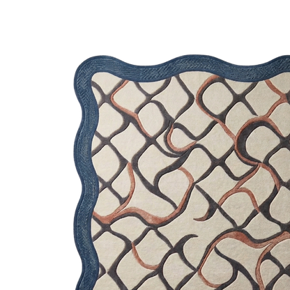 A close-up of a patterned textile or rug corner with a scalloped dark blue border, cream background, and interlocking wavy lines in black and warm brown.