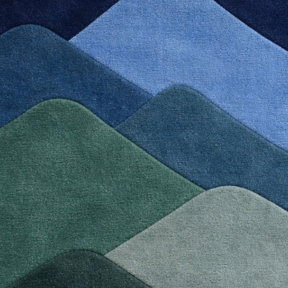 A close-up of layered, rounded mountain-like shapes in shades of blue, green, and pale gray, showing a soft textured surface.