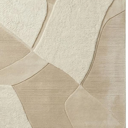 A close-up of a beige and cream textured rug with a geometric patchwork design, featuring a mix of plush, looped, and ribbed textures.