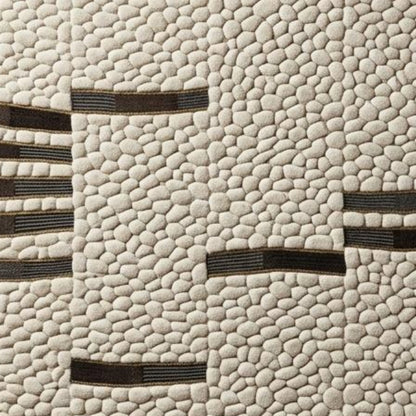 A close-up of a textured fabric or wallpaper featuring a cream-colored pebble pattern with dark brown horizontal stripe accents.
