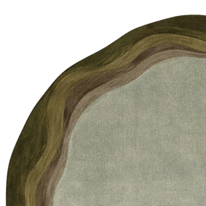 A close-up of a round rug with a textured, layered organic border in olive green, brown, and beige, surrounding a light gray-green center on a white background.